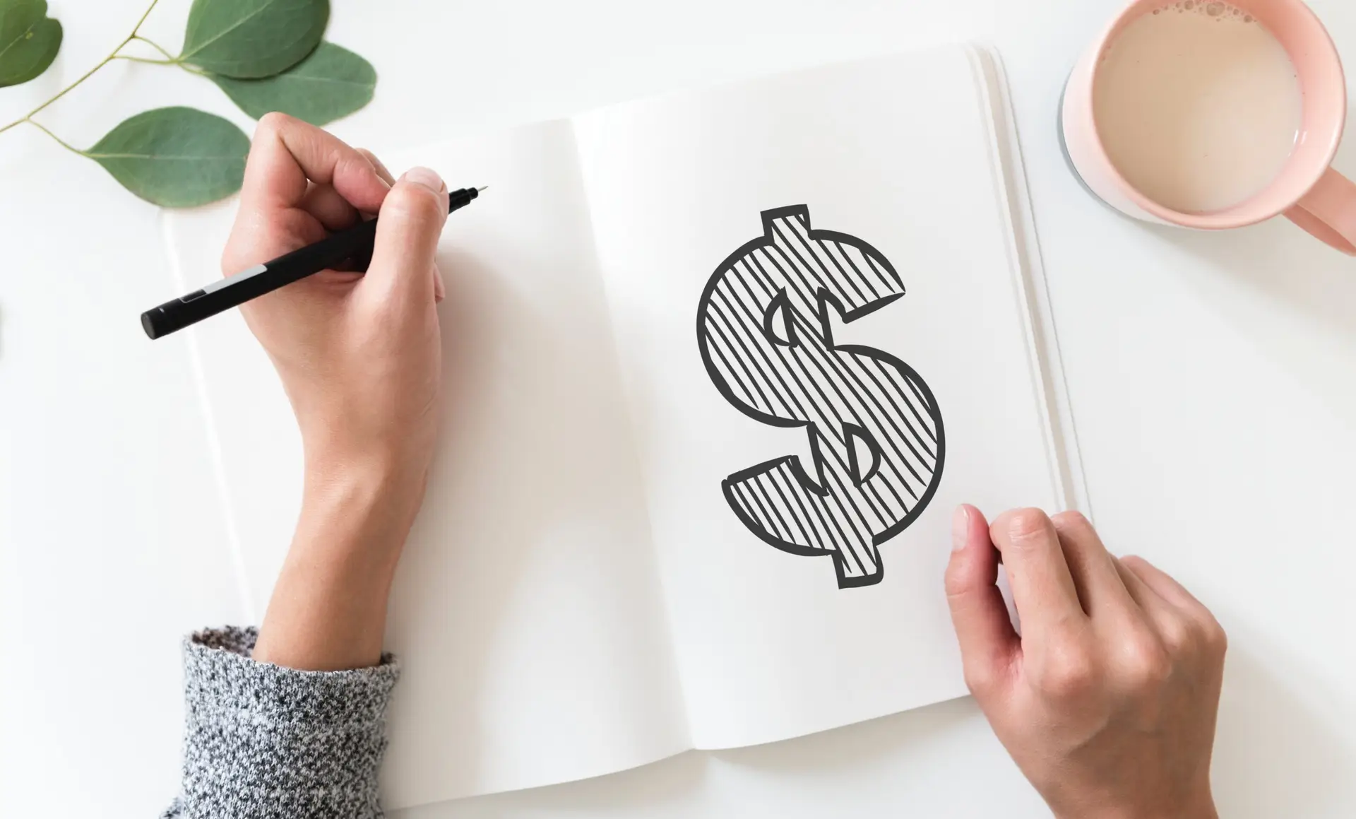 Picture of a hand with a pen writing in a book. Inside the book there is a big dollar sign.