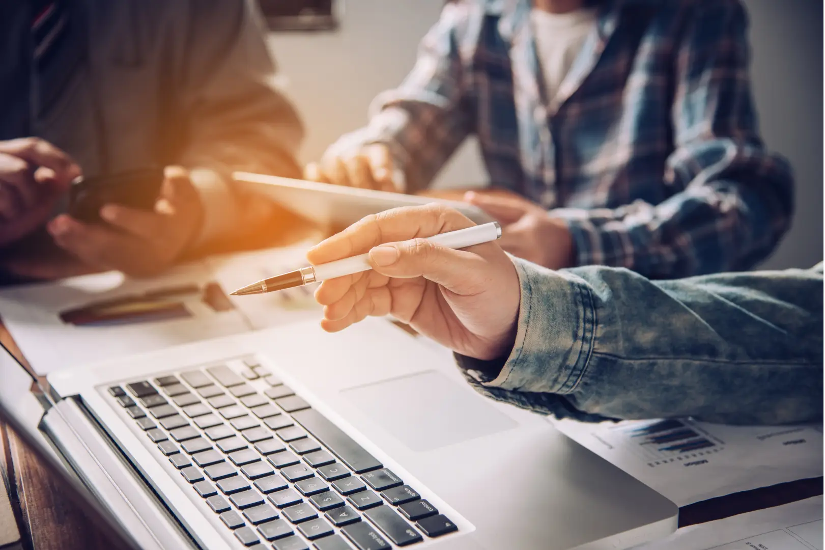 People around a table and one of them pointing with a pen on the laptop-screen.