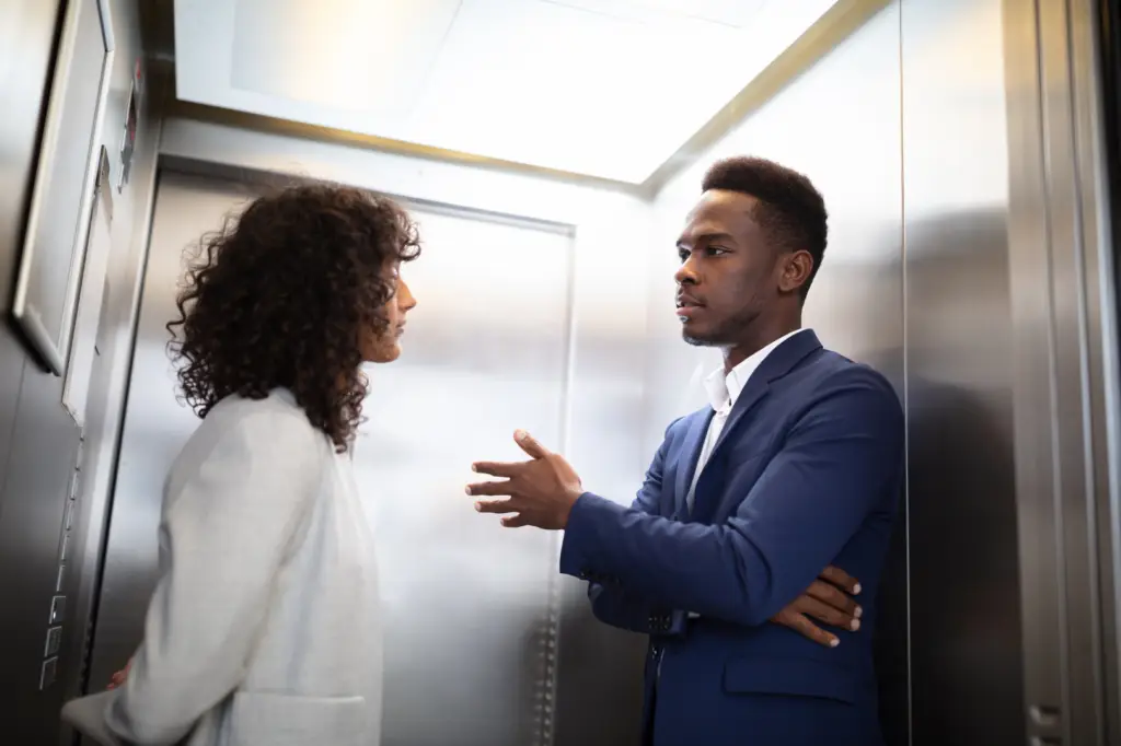 Two persons standing in a elevator. One of them are doing the elevator pitch to the other.