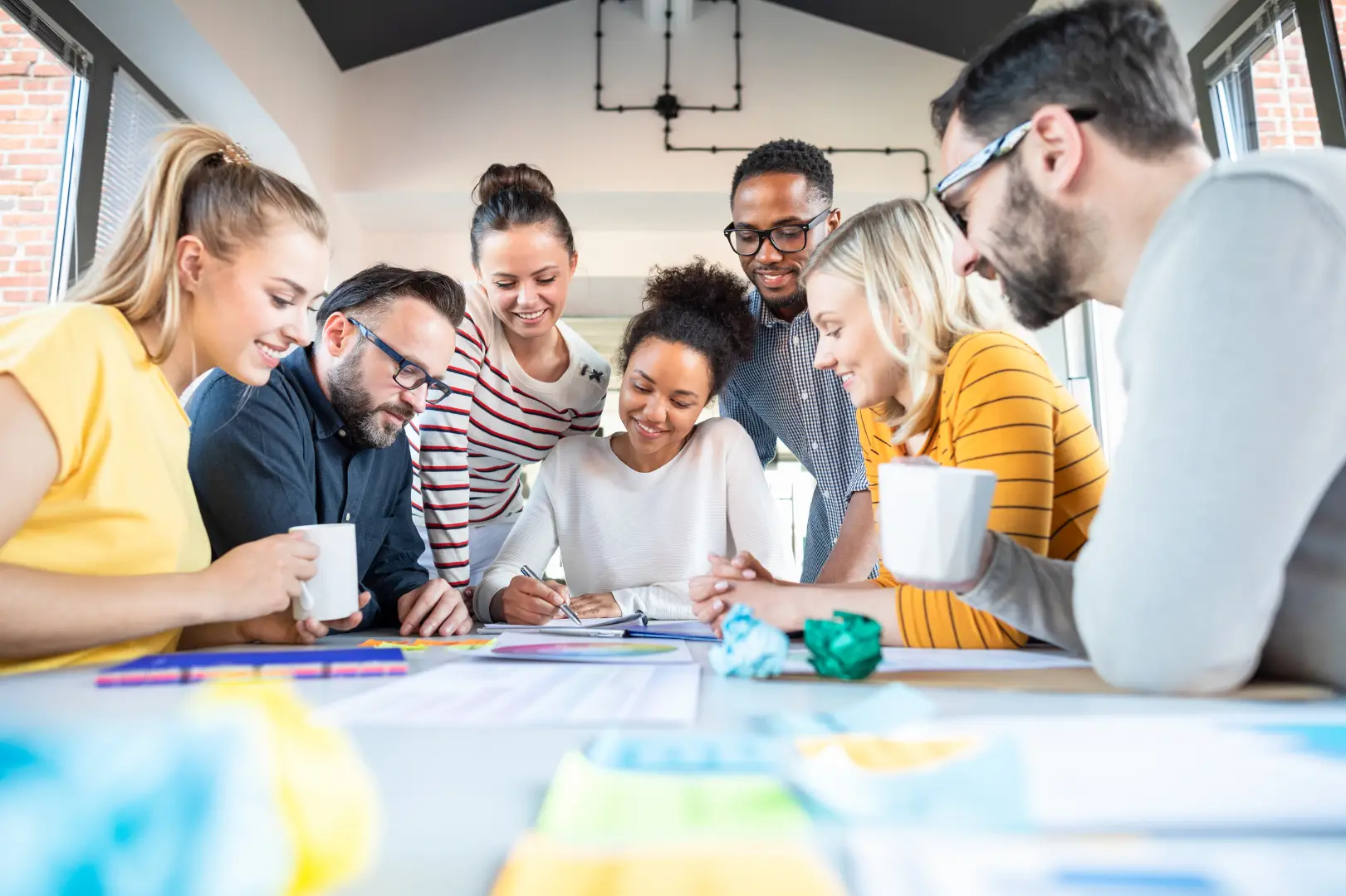 A diverse team sitting around a table and working together with diagrams and customer journey maps.