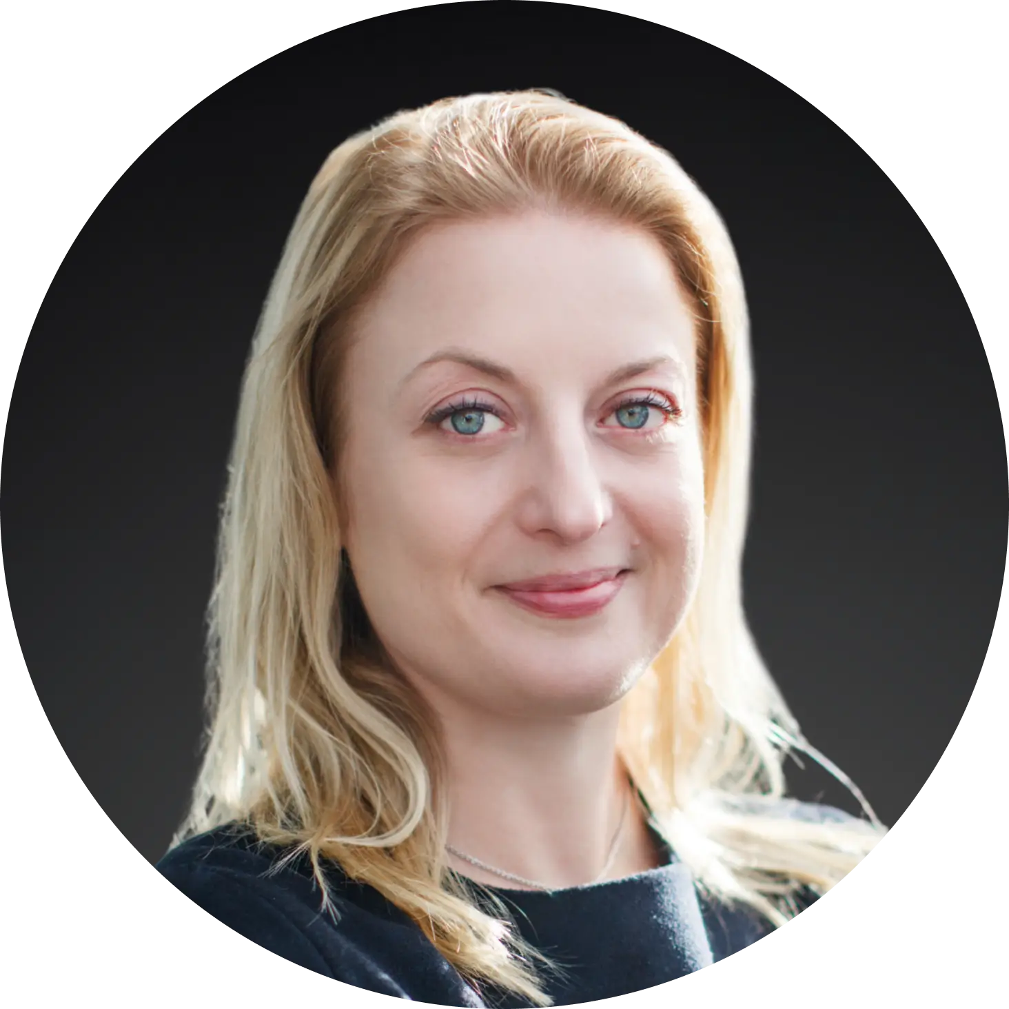 Portrait of Gül Heper-Jämterud, a blonde woman with blue eyes, smiling slightly and wearing a dark top. Neutral background with soft lighting.